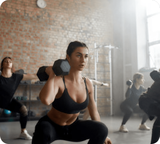 Grua duke bërë squats me peshë në një palestër grupore – transformim personal dhe fitnes me Transformohu per humbje peshe dhe transformim